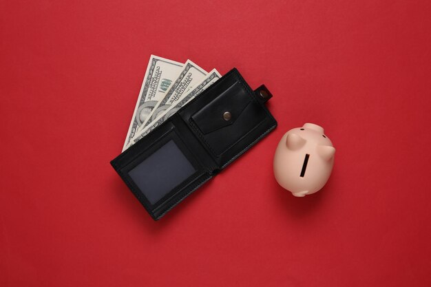 Leather wallet with one hundred dollar bills and a piggy bank on a red background Saving money