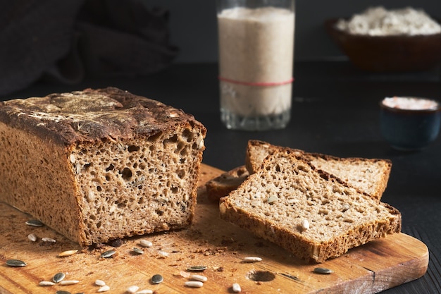 Leavened bread, whole grain rye bread with pumpkin and sunflower seeds. Leaven starter on table. Authentic sourdough homemade bread-organic bio product. Handcrafted product, slices of bread on board