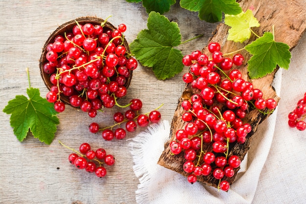 The leaves and berries of red currant on piece of old wood and in a bowl, top view