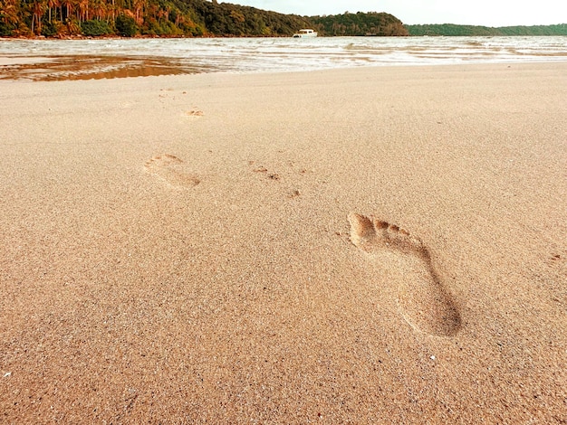 Leaving footprint on the sand Closeup footprint from foot step walking on the sandy beach on sea and rock island view with copy space Beach travel summer background concept