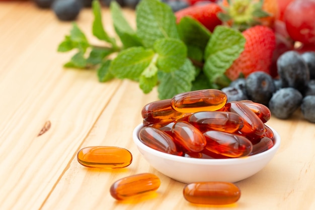 Lecithin gel vitamin supplement capsules in a small cup on the wooden table with variety fruit