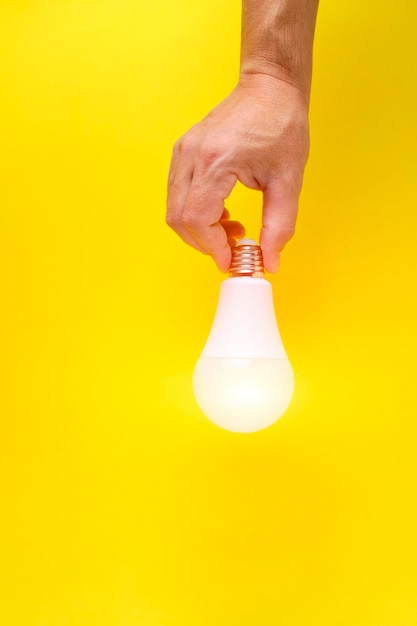 LED eco friendly light bulb in hand on yellow background