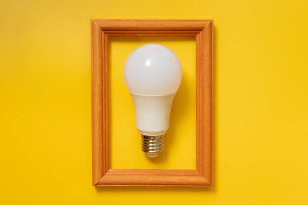 Photo led energy saving bulb in wooden frame on yellow background