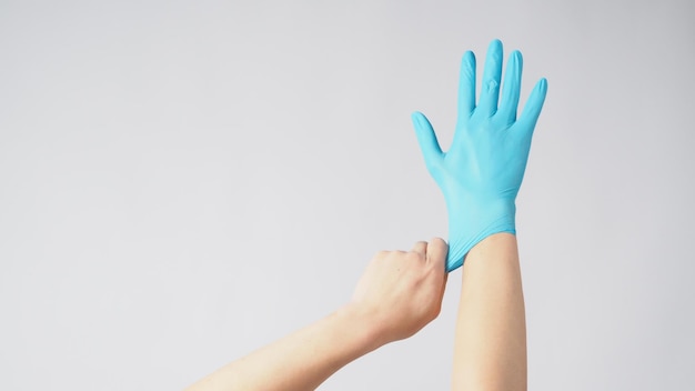 Left hand is pulling right hand with blue latex gloves on white background.