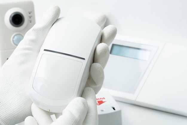 The left hand of a man in a white glove holds a motion sensor of security systems