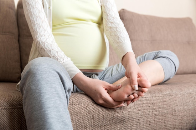 Leg cramps during pregnancy Closeup of hands massaging swollen foot while sitting on sofa