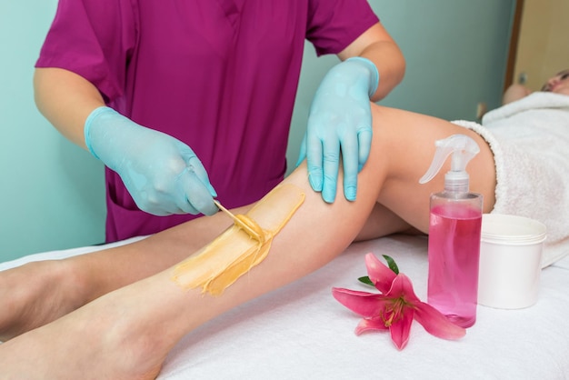 Leg sugaring A beautician makes a sugar paste depilation of a woman's legs in a beauty salon Female aesthetic cosmetology Apply sugar paste with a wooden spatula