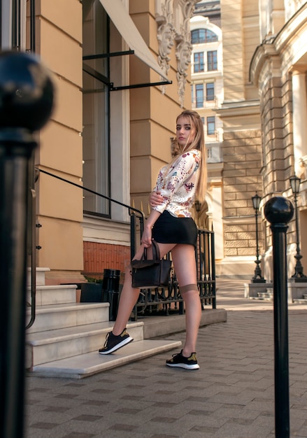 Leggy blonde with a bag in her hands posing near the boutique