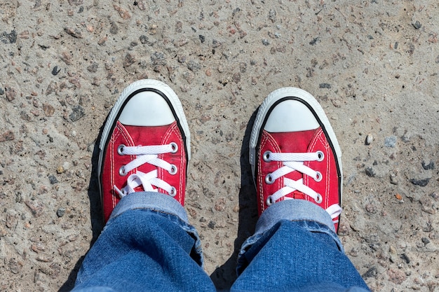 Legs in blue jeans and red sneakers on the pavement on a sunny day