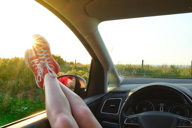 Legs of a girl in red sneakers sticking out of a car window