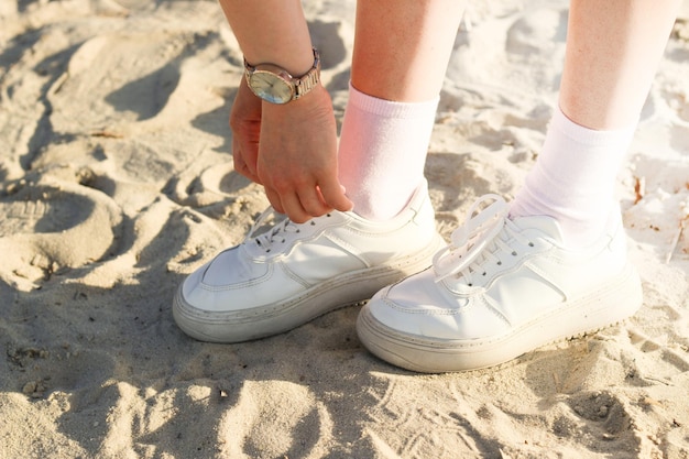 Legs of a girl in a skirt in fashionable sneakers on the sand the image is taken for a walk