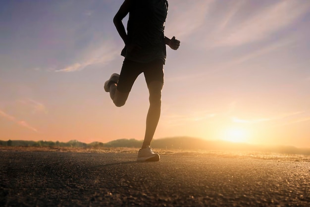 Legs of a male runner running on the road at sunset.