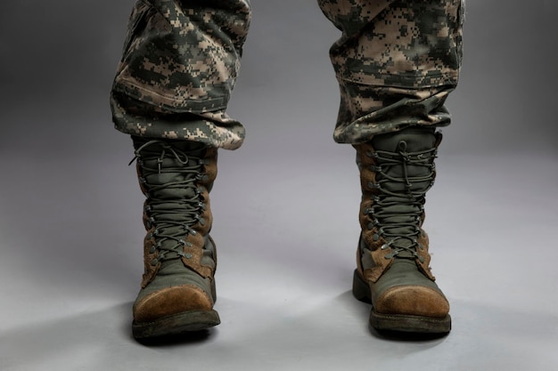 Legs of a man in a camouflage suit and army boots. Political conflicts and a turbulent military environment. Close-up. Gray background.