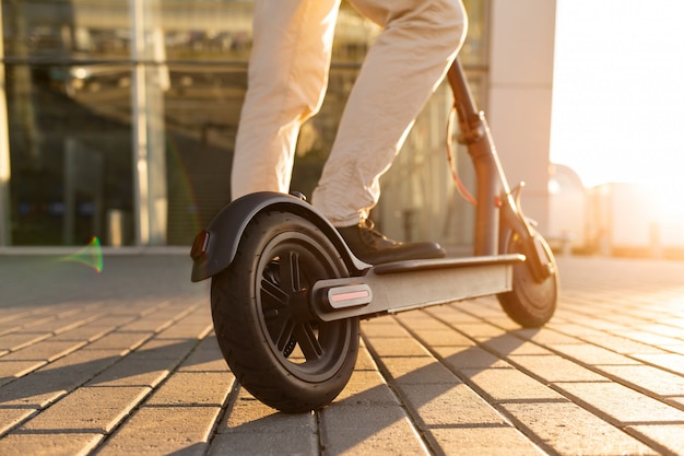 Legs of a man standing on e-scooter parked on sidewalk