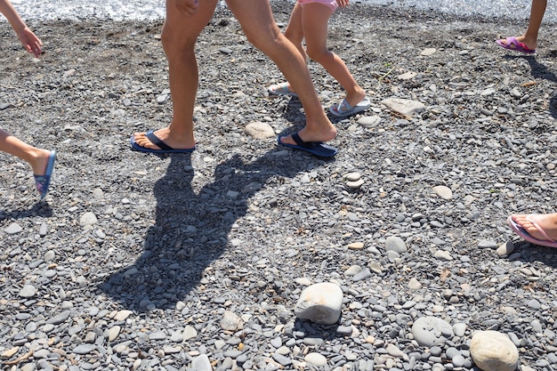 Legs of tourists walking along the pebbly seashore in summer. Travel and tourism.