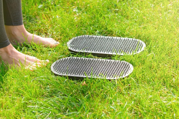 Legs of a woman standing on the grass next to sadhu yoga boards with nails outdoors