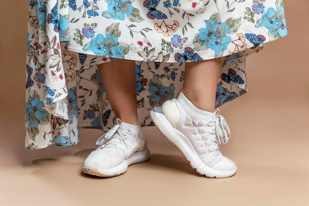 Legs of a woman in white sneakers and a long romantic dress Fashion Style Closeup Beigebrown background