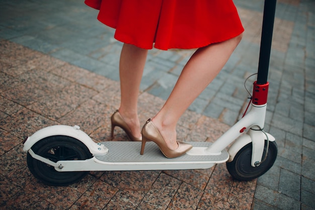 Legs of woman with electric scooter in red dress at the city