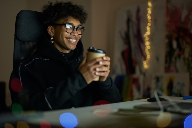 Leisure activities happy young guy with piercing wearing glasses holding disposable cup of coffee