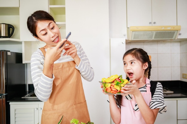 Leisure activity in a kitchen at home Mom and little girl enjoy takes a photo of vegetable salad