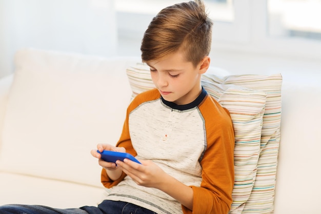 leisure, children, technology, internet addiction and people concept - boy with smartphone texting message or playing game at home