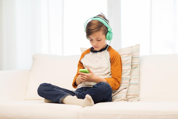 leisure, children, technology and people concept - boy with smartphone and headphones listening to music or playing game at home