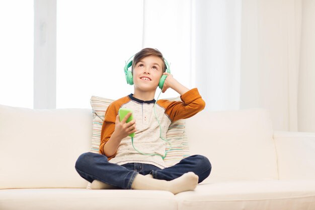 leisure, children, technology and people concept - smiling boy with smartphone and headphones listening to music at home