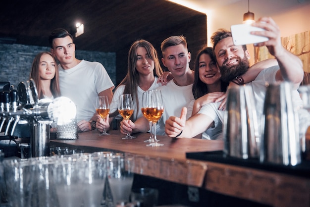 Leisure and communication concept. Group of happy smiling friends enjoying drinks and talking at bar or pub and making a selfie photo.