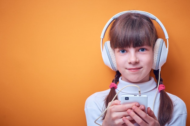 Leisure and entertainment , Caucasian teen girl listening to music with headphones using the phone on a colored