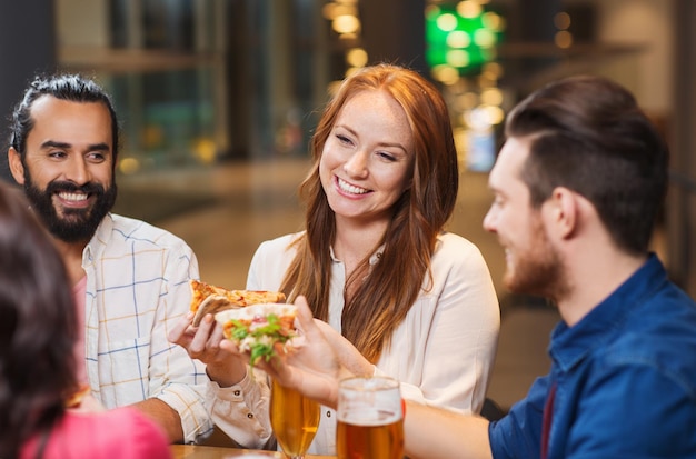 leisure, food and drinks, people and holidays concept - smiling friends eating pizza and drinking beer at restaurant or pub