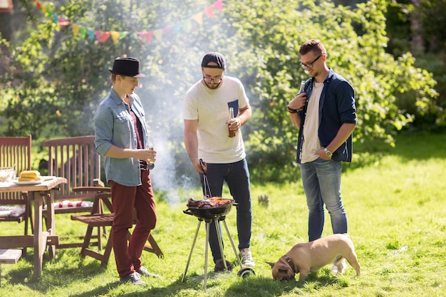 leisure, food, people, friendship and holidays concept - happy friends cooking meat on barbecue grill and drinking beer at summer outdoor party