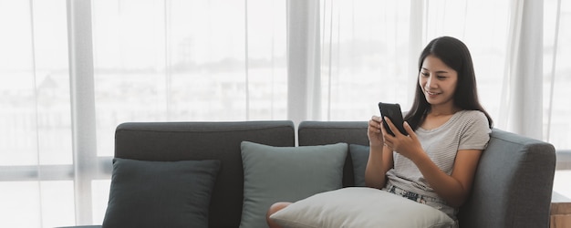 Leisure from home and online shopping concept, Happy asian woman relax and using mobile phone on sofa in living room at home