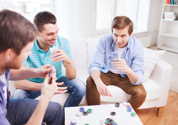 leisure, games, friendship, gambling and entertainment - three smiling male friends playing cards at home