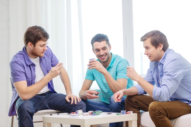 leisure, games and lifestyle concept - happy three male friends playing poker at home