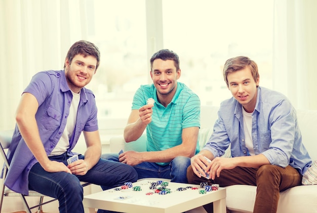 leisure, games and lifestyle concept - happy three male friends playing poker at home