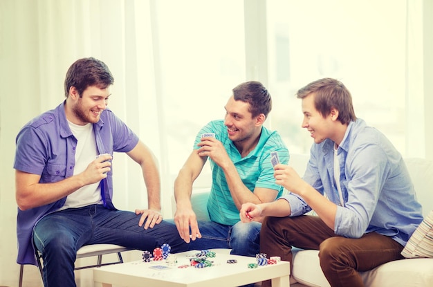 leisure, games and lifestyle concept - happy three male friends playing poker at home