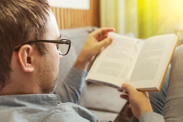 Leisure literature and people concept man sitting on sofa and reading book at home reader is reading a novel A student is studying a textbook The guy is holding a book in his hand