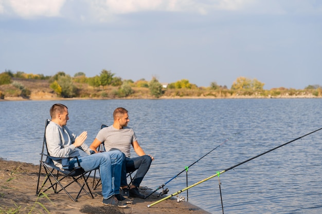 Leisure and people concept. Happy friends with fishing rods on pier by lakeside.