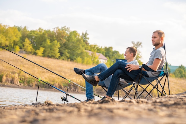 Leisure and people concept. Happy friends with fishing rods on pier by lakeside.