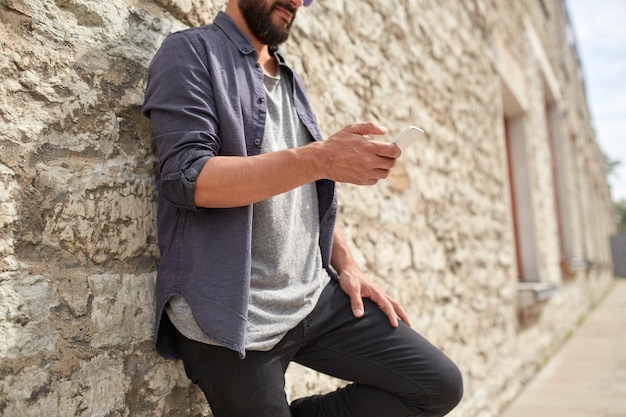 leisure, technology, communication and people concept - close up of man with smartphone at stone wall on street