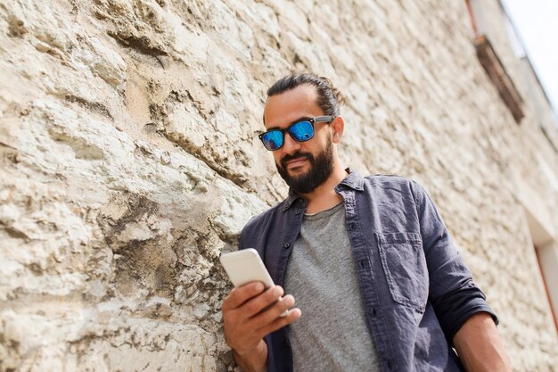 leisure, technology, communication and people concept - man in sunglasses texting message on smartphone at stone wall