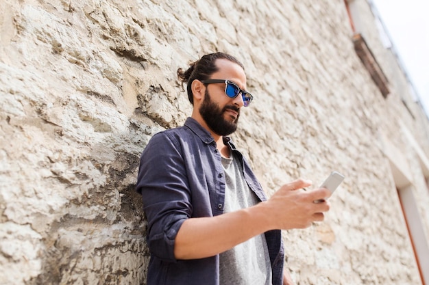 leisure, technology, communication and people concept - man in sunglasses texting message on smartphone at stone wall