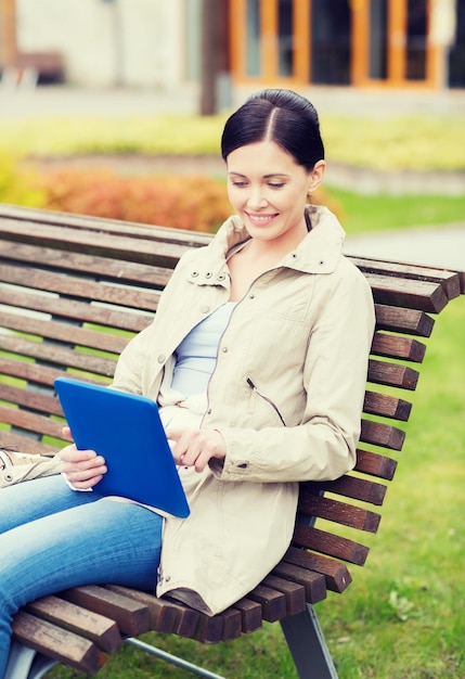 leisure, technology, communication and people concept - smiling woman with tablet pc computer sitting on bench in park