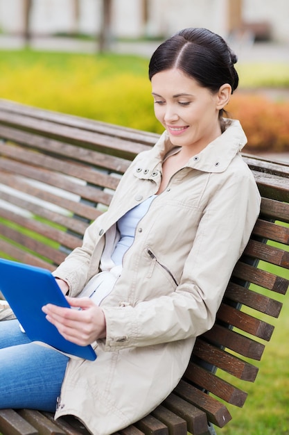 leisure, technology, communication and people concept - smiling woman with tablet pc computer sitting on bench in park