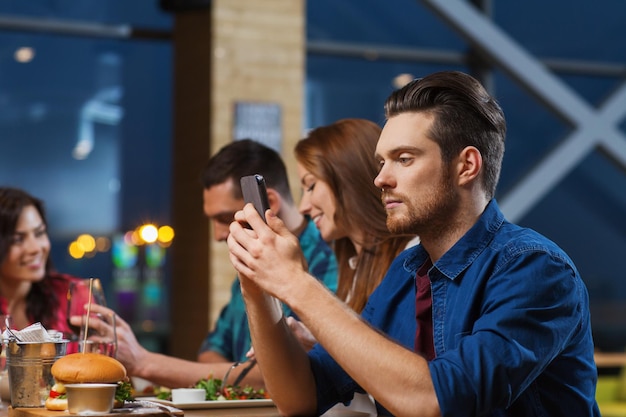 leisure, technology, internet addiction, lifestyle and people concept - man with smartphone and friends at restaurant