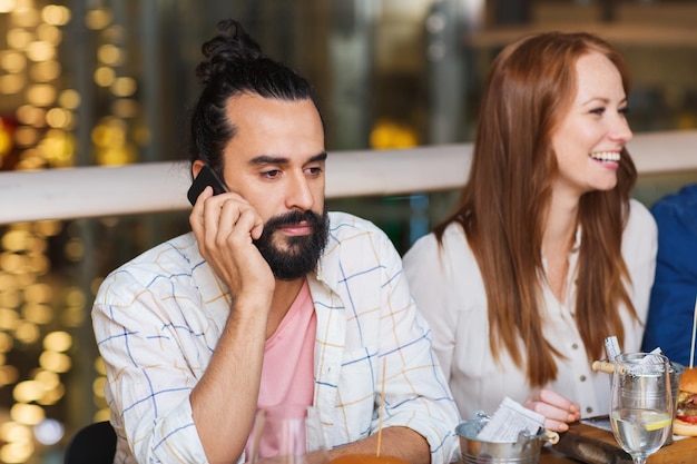 leisure, technology, lifestyle and people concept - man with smartphone and friends dining at restaurant