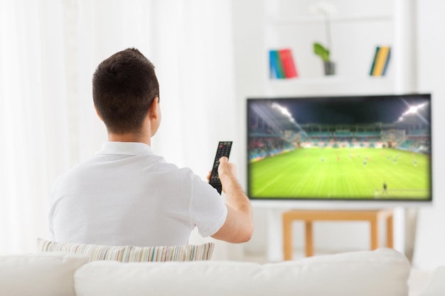 leisure, technology, sport, entertainment and people concept - man with remote control watching football or soccer game on tv at home