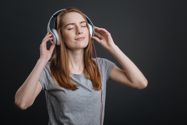 Leisure with pleasure. Dreamy graceful lively girl testing her new headphones while listening to her favorite song and looking delighted