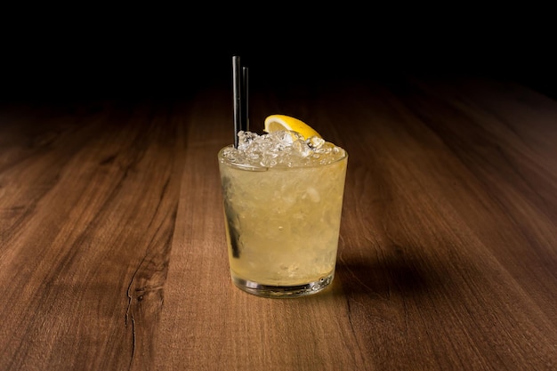 lemon alcoholic cocktail with ice a slice of lemon and a straw on a dark background in a bar