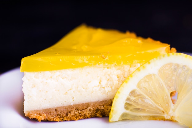 Lemon cheesecake on black background decorated with lemon zest close up